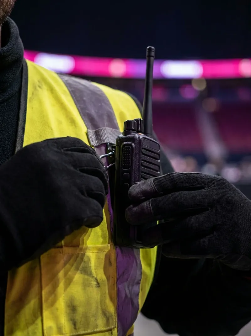 Mani che agganciano la radio al gilet alta visibilità prima del turno