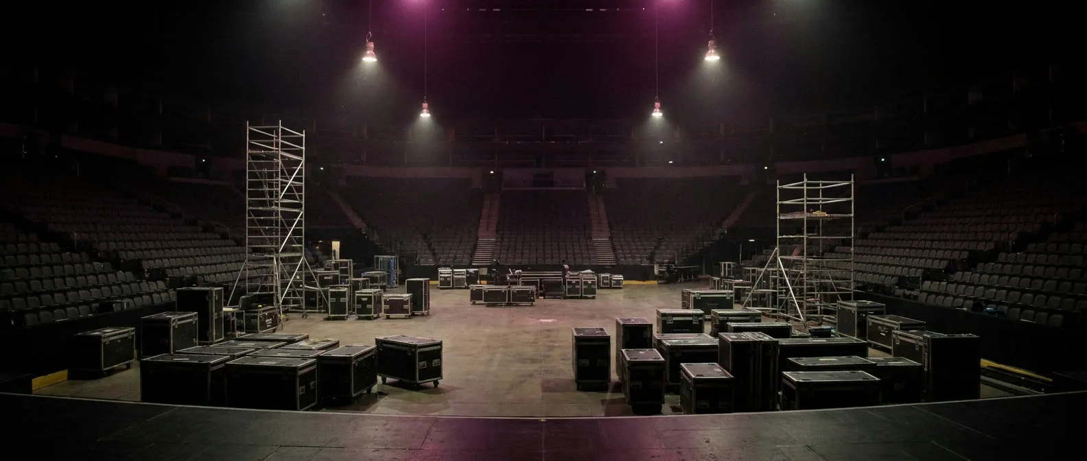 Arena vuota vista dal palco durante il load-in, tra flight case e torri di scaffolding