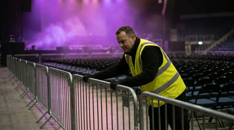 Operatore in gilet alta visibilità che ispeziona la transenna in un'arena vuota